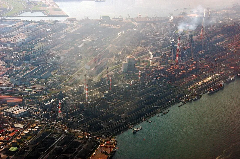 海ぞいに広がる製鉄所。溶鉱炉や工場群、原料置き場が港に沿ってならぶ